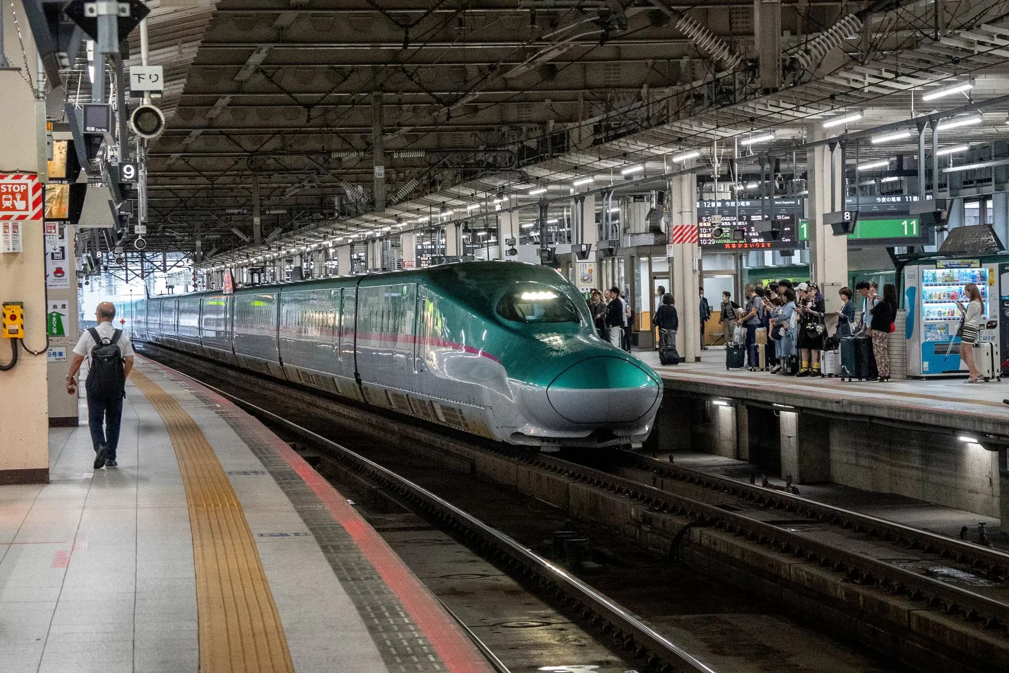 A green Shinkansen train at a busy station platform